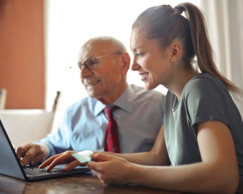 young woman helping senior man with payment on internet using laptop