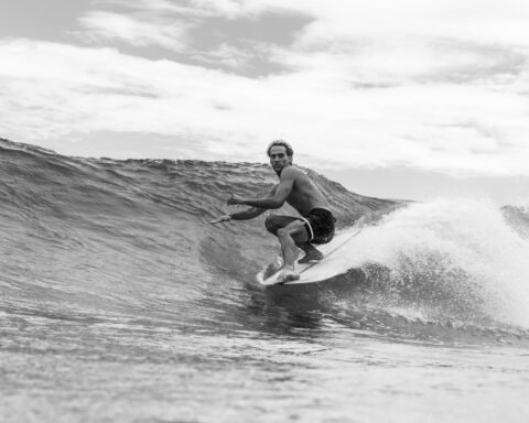 grayscale photo of a shirtless man surfing on sea waves