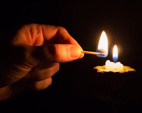 person holding match stick with fire in front of candle with fire