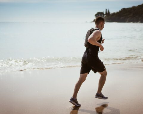 man wearing black tank top and running on seashore