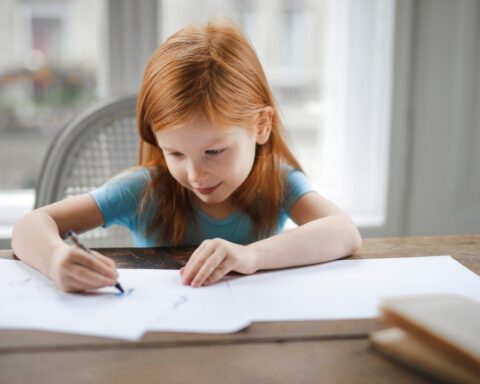 diligent small girl drawing on paper in light living room at home