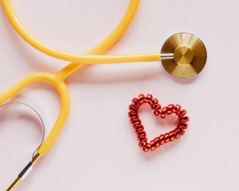 stethoscope near decorative coil tie in heart shape on pink surface