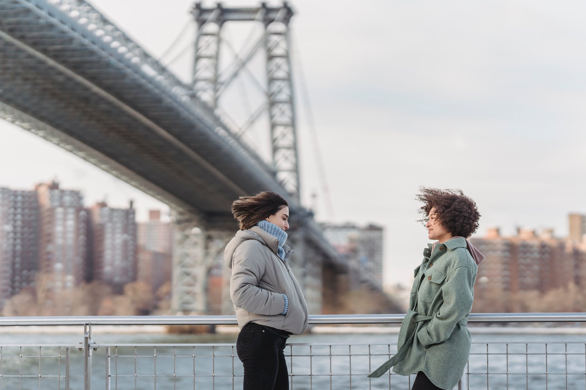 women in outerwear chatting on city embankment on windy day