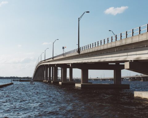 brown concrete bridge above body of water under blue sky and white clouds