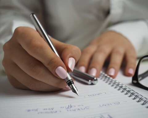 woman in white long sleeved shirt holding a pen writing on a paper